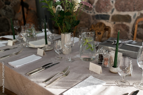 Fotografija Elegant rustic tablescape with linen tablecloth, glassware, candles, and wildflower centerpiece set for intimate fine dining in a stone-walled venue