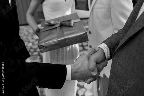 Fotografie Elegant black-and-white wedding moment as a guest offers a gift while a formal handshake seals congratulations, symbolizing respect, tradition, and partnership