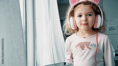 Child listening to music on headphones at home near window