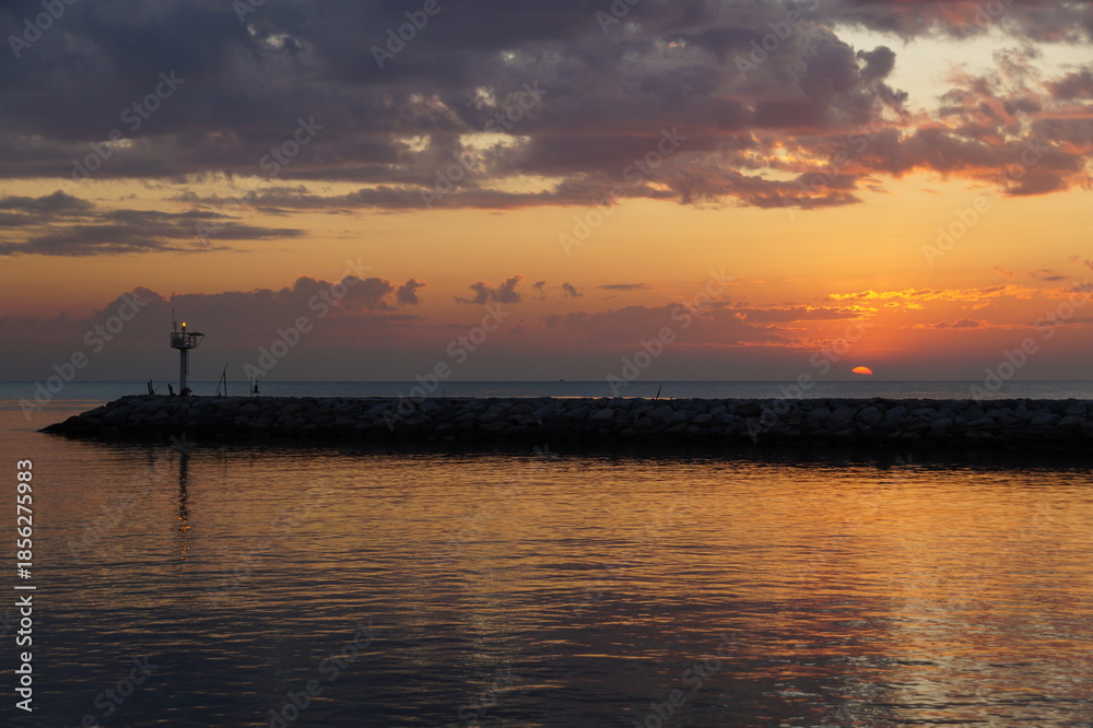 Naklejka premium The red ball of a huge sun rises from the horizon. The sky is painted a bright orange. Summer, morning twilight. Golden dawn on the sea.