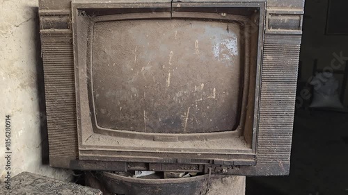 Old vintage television set with a worn screen and dusty exterior placed against a neutral background in a room