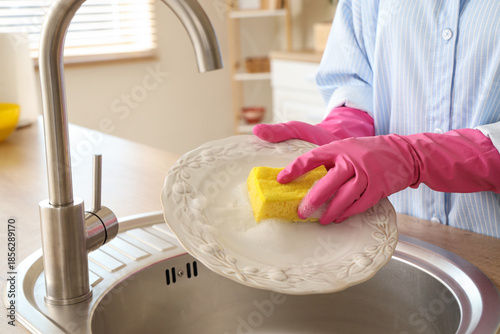 Fotografia Young woman washing dishes with housework sponge in kitchen sink