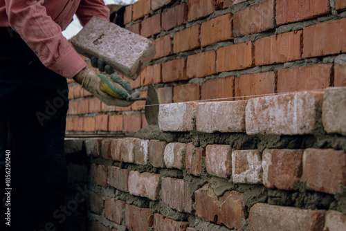 Worker laying brick on mortar during wall construction