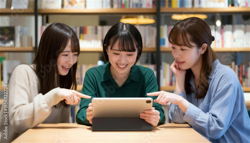 本棚のある空間でタブレットを囲んで相談する日本人女性3人