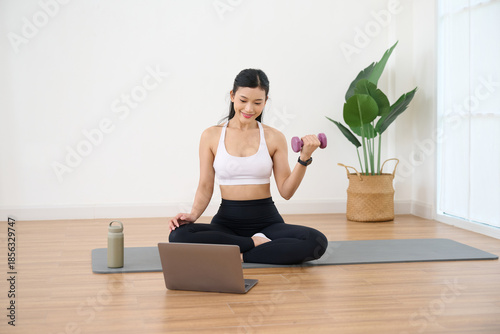 Woman is working out with dumbbell at home while watching exercise instructions on a laptop