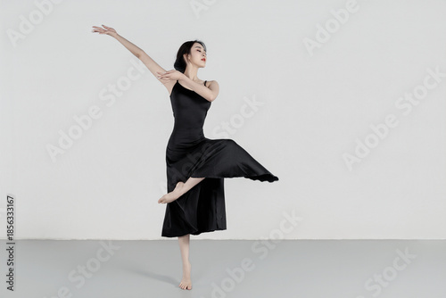 A beautiful girl wearing a black long dress is practicing dance in the dance studio