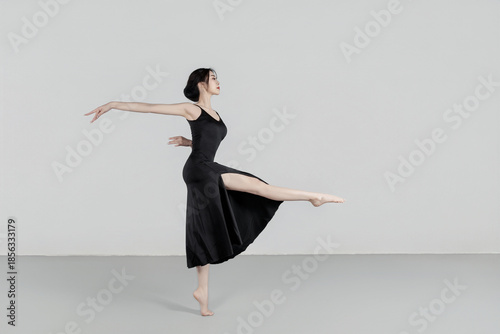 A beautiful girl wearing a black long dress is practicing dance in the dance studio