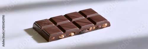 Exquisite dark chocolate bar generously studded with crunchy roasted hazelnuts, artfully presented on a pristine white surface under soft, natural studio lighting