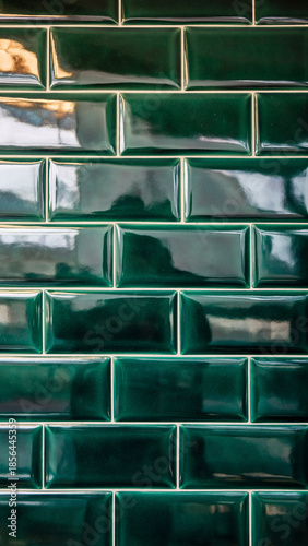 Vertical close-up of glossy, green ceramic subway tiles arranged in a traditional running bond pattern with contrasting white grout. The beveled edges of the vintage-style tiles catch reflections, 