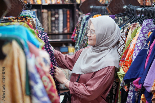 Asian woman shopping for traditional Indonesian batik garments in a fashion store.
