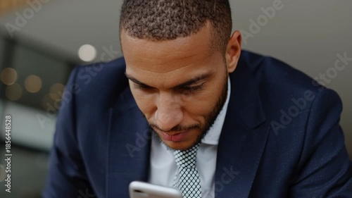 A businessman in a suit focuses on his smartphone and tablet in a sleek office. He appears engaged and attentive, balancing technology and productivity in his daily tasks