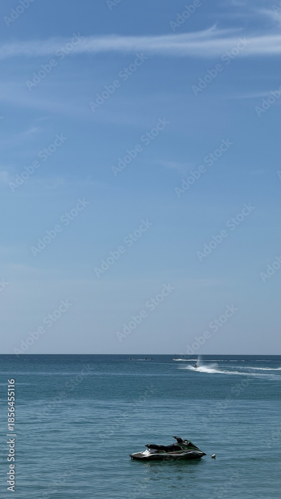 Naklejka premium Jet ski on a calm blue sea under a clear blue sky. Peaceful seascape with minimal composition, travel and summer vacation concept, vertical photo with copy space