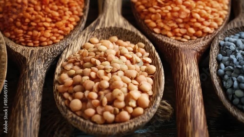 A captivating close-up highlights an inviting assortment of dried legumes, meticulously arranged in a collection of rustic wooden spoons. The shot emphasizes the rich variety of colors and textures, s