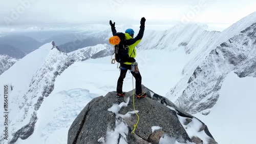 Climber at mountain peak, arms raised, surrounded by snowy peaks and clouds