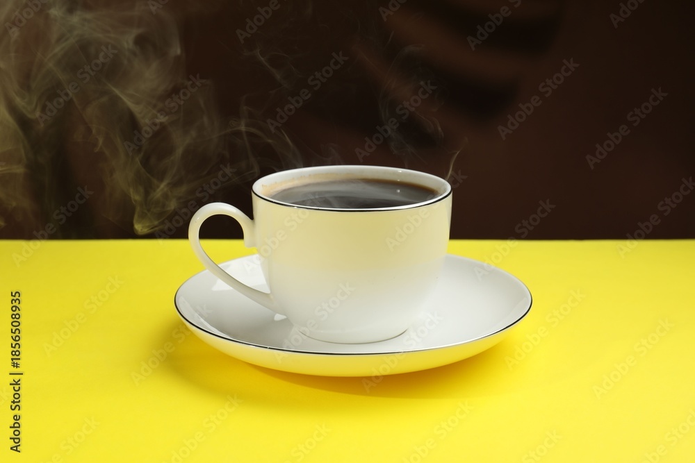 Obraz premium Aromatic coffee in cup on yellow table against dark background