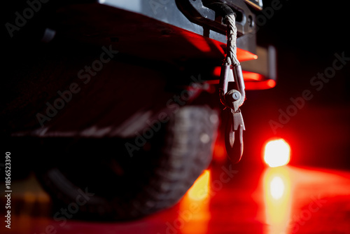 Heavy duty towing hook and cable mounted on vehicle rear with rugged tire and red warning light glow, industrial transport safety concept