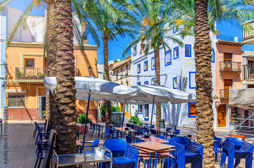 Fototapeta premium Old town Calpe city historical centre with street restaurant outdoor cafe on square Plaza Espana, houses colorful traditional buildings in sunny day, Calp Casco Antiguo, Valencian Community, Spain