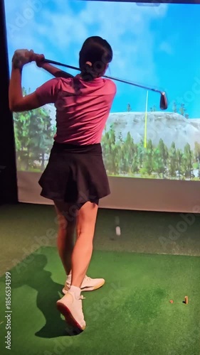 Woman practices golfing swing indoors at virtual golf range in evening time setting