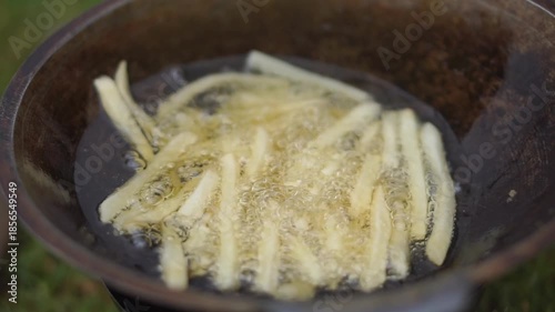 Thinly sliced potatoes frying in hot oil in a traditional pan.