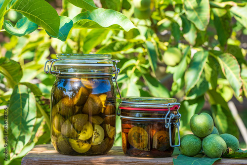 Sliced unripe walnuts in alcohol in a glass jar, to prepare homemade tincture, closeup. Tincture of green walnuts in a glass jar on a table in the summer garden