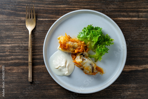 Two delicious cabbage rolls stuffed with meat and rice on a plate along with sour cream and lettuce, closeup, top view
