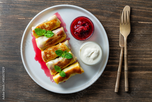 Fried rolled pancakes stuffed with cottage cheese and cherry, sweet dessert on plate, closeup, top view. Homemade baking. Delicious fast food for breakfast. Wrapped pancakes with sour cream and jam