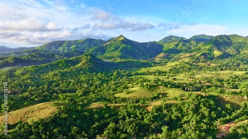 A landscape of mountain peaks against a cloudy sky. A mountain valley in the rays of the morning sun. The vibrant tropical nature of the Dominican Republic. Multicolored hills with green meadow grass.
