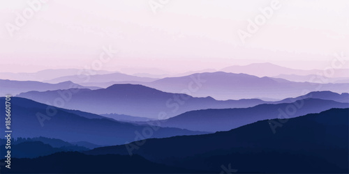 A misty blue morning fog blankets the mountain valley at sunrise as the sun glows over a scenic forest landscape of hills and clouds at dawn