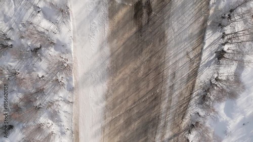 Aerial fly over ski slope with melting snow revealing large brown soil patches and tracks, symbolizing climate change, global warming and winter season decline. Early end or late start of ski season