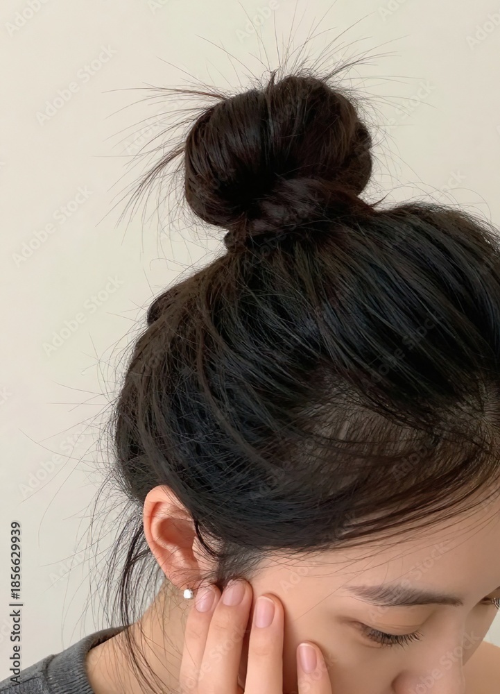 Fototapeta premium a close-up view of a woman with their dark hair styled in a bun, with their hand near their face, focusing on the hair details.
