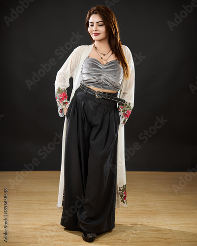 Full-length studio portrait of an elegant woman standing confidently with hands in pockets, wearing a modern outfit against a dark background. Concept of confidence, style, independence, and contempor