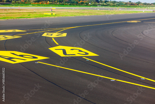 Yellow painted hold position markings and taxiway designations on dark asphalt at an airfield. Aeronautical paint and the dark, textured runway pavement