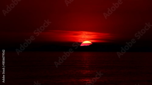 Time-lapse of a large round sun setting slowly over the calm sea at the horizon
