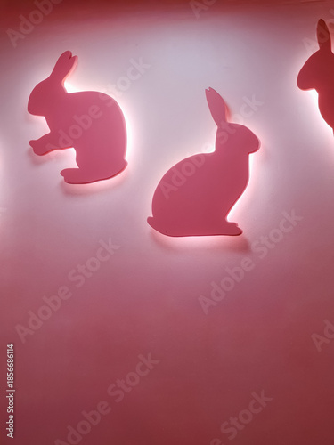 Highlighted pink silhouettes of rabbits mounted on a vibrant pink wall, creating a modern, abstract, and charming design