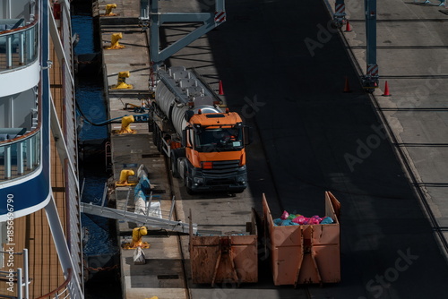 Service tanker truck at cruise terminal pier beside docked ship