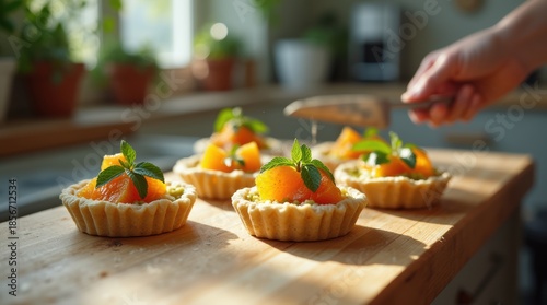 Delicious homemade fruit tarts being garnished with fresh mint leaves on a wooden board in a sunlit kitchen.