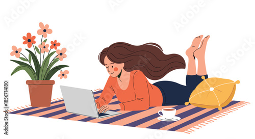Young woman comfortably working on her laptop while lying on a striped rug at home, with a potted plant and coffee nearby.