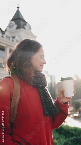 A young woman enjoys her takeaway coffee while walking through a European city on a warm autumn day
