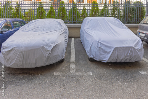 Canvas Print Two Cars Under Tarpaulin Cover at Street Parking Protect From Weather and Elemen