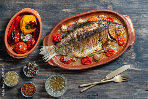 Delicious baked big fish crucian carp with spices in a clay plate and fried vegetables, closeup, top view