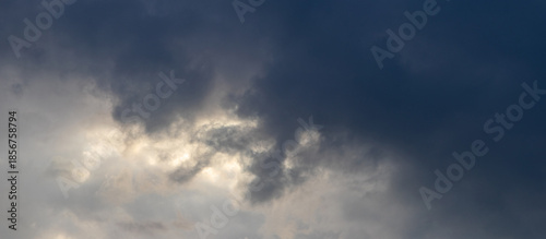 Dramatic dark storm sky with dense black clouds and bright light through clouds, atmospheric weather background before thunderstorm