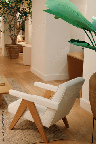 Modern white armchair with wooden legs placed in a warm minimalist interior. Stylish seating furniture for living room hotel lobby or showroom interior design and lifestyle concepts.