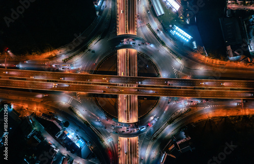 Stunning top-down aerial view of a complex highway interchange at night, featuring vibrant long-exposure traffic light trails in Nonthaburi, Thailand.