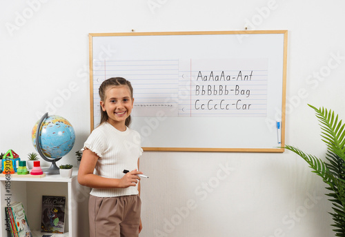 Tableau sur toile Cheerful girl studies alphabet and handwriting using a magnetic wall board