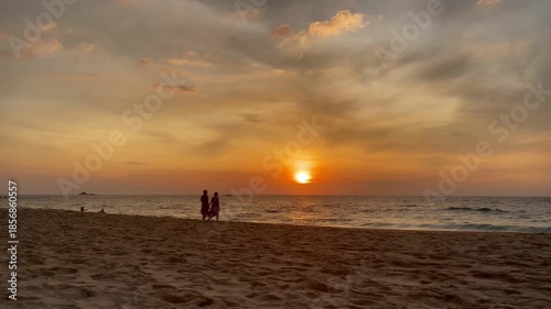 Silhouetted couple walking along a sandy beach at sunset with calm ocean and warm sky tones, tropical travel and romance, travel, vacation, relaxation, summer lifestyle, and peaceful moment concepts
