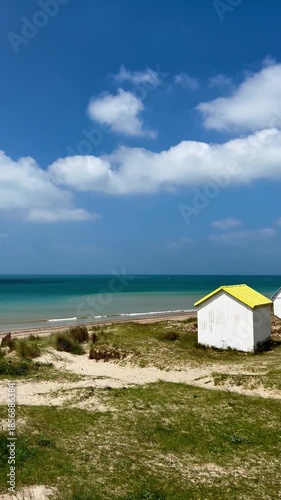 Wallpaper Mural Colourful Beach Cabins in dunes at Gouville-sur-Mer, Normandy, France. Atlantic ocean. Colorful beach cabins with red, blue, and yellow roofs stand amidst sandy dunes and sparse grass.  Torontodigital.ca
