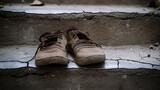Worn, vintage shoes rest on cracked steps. The subdued lighting and textures evoke memories of bygone eras and stories etched into time. Timeless comfort and resilience.