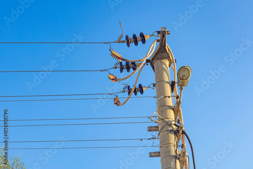 Billede på lærred Concrete utility pole with electrical wires, insulators and street lamp against clear blue sky