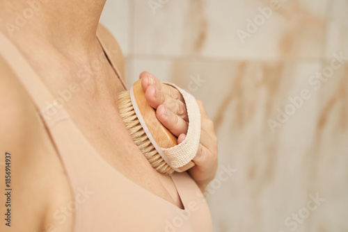 Photos female Caucasian mature body brushing chest selfcare ritual at home bathroom drybrush skincare routine with natural bristle brush promoting circulation relaxation and body acceptance