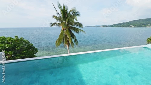 View from luxury villa at sunny day, sun loungers for sunbathing, umbrellas from the sun, pillows for swimming in the pool, palm tree on background